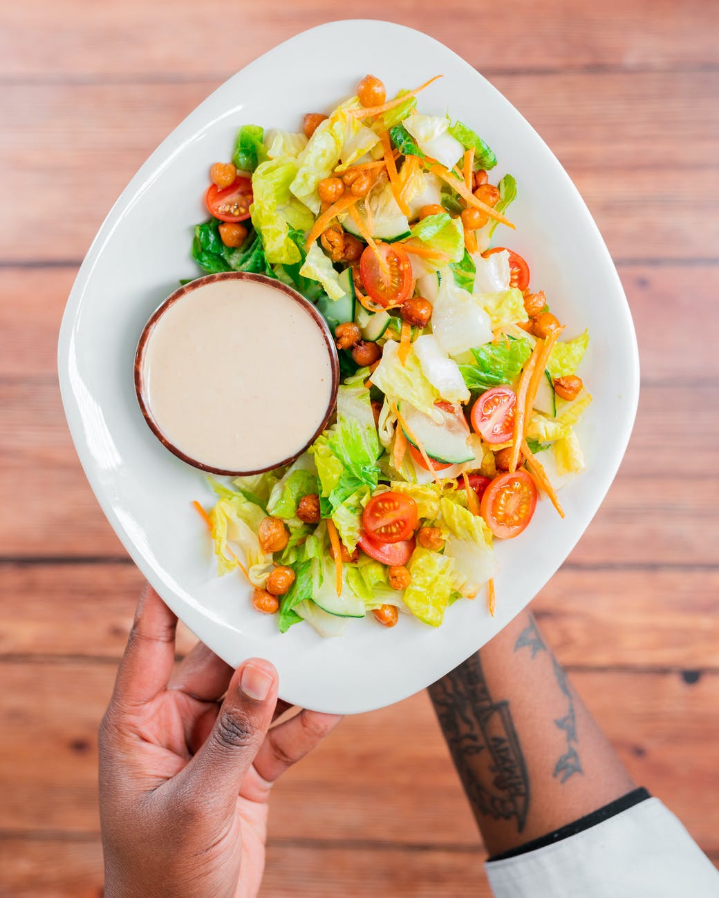 hands holding plate with salad and dressing
