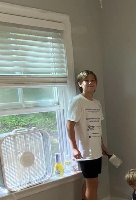 a boy standing by a window with a paint brush